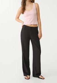 Lichtroze mouwloos topje gecombineerd met zwarte broek met wijde pijpen. Het topje heeft een ronde halslijn; de broek is gemaakt van een gladde stof met een getailleerde pasvorm.