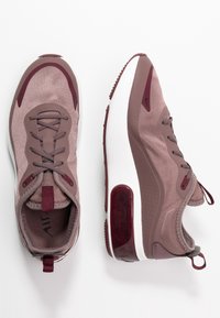 Ett par mauve- och burgundy-färgade atletiska sneakers med vita sulor, en sko sett uppifrån och den andra i profilvy mot vit bakgrund.