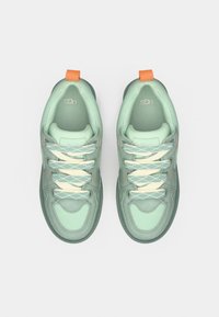 Chaussures de sport vertes dotées d'une tige en mesh, d'accents texturés, de lacets blancs avec un motif, et d'une languette de talon orange.