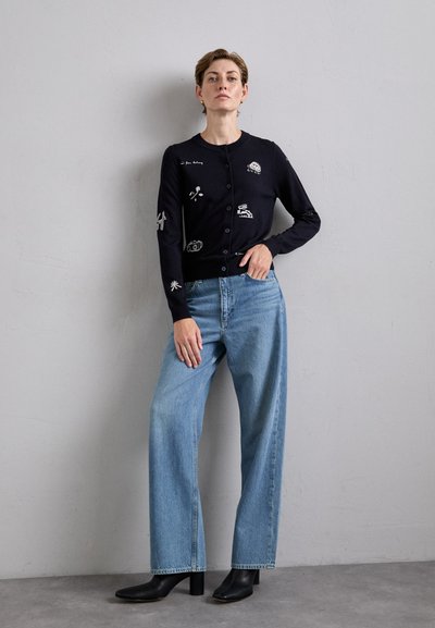 Mörkblå stickad cardigan med vita broderade motiv, rund hals, långa ärmar och framsidan med knappknäppning. Matchad med ljusblå vida jeans och svarta klackstövlar.