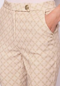 Pantaloni beige con motivo a diamante sottile, tasca frontale e chiusura con bottone dorato in vita.