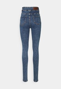 Vaqueros ajustados de mezclilla azul con cintura alta, que presentan una textura suave, dos bolsillos traseros y una parche de cuero marrón en la cintura.