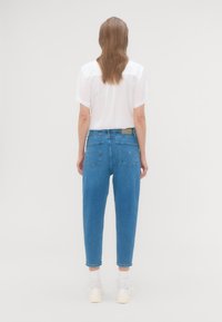 Kék farmer boyfriend nadrág laza fazonnal, ötpocket dizájnnal és világos mosással. Rövid ujjú fehér toppal párosítva.