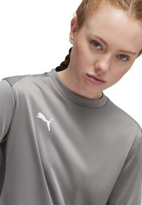Maglietta sportiva grigia realizzata in tessuto liscio, con collo rotondo e logo Puma bianco sul petto. Presenta un design semplice.