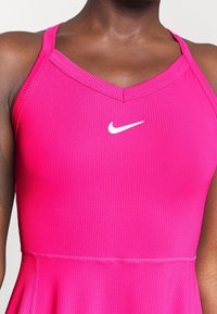 Débardeur rose à côtes avec un décolleté en V et des bretelles réglables. Présente un logo Nike blanc sur la poitrine et un bas évasé.