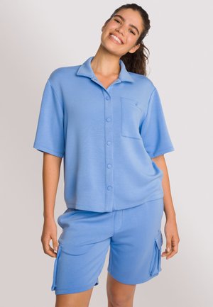 Helderblauw lounge set met een kortemouwen, knoopsluiting bovenstuk met een zak en bijpassende shorts met een zijzak voor opbergruimte.