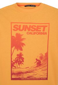 T-shirt di cotone giallo con una grafica rossa che presenta "SUNSET CALIFORNIA" e una silhouette di un surfista contro palme e onde.