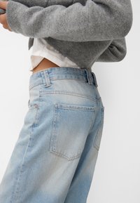 Light blue denim jeans with a fitted waist, two back pockets, and a slight fade effect. Paired with a gray sweater and white shirt.