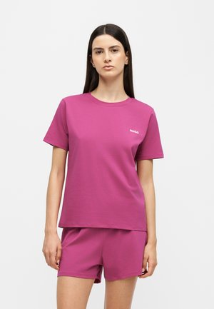 Woman with straight dark hair wears a matching magenta t-shirt and shorts set with a small white "HUGO" logo on the chest.