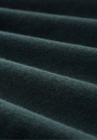 Tissu tricoté vert foncé plié en rainures parallèles douces, mettant en valeur la texture et les fibres fines.