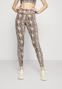 Legíny s hadím vzorem v béžové a černé barvě, vyrobené z elastického materiálu. Mají vysoký pas a přiléhavý střih. Sada světlých tenisek.