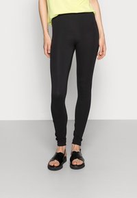Leggings pretos com um tecido suave e elástico, design ajustado e corte até ao tornozelo, acompanhados de sandálias pretas planas.