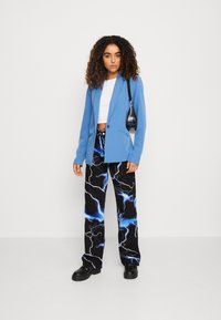 Blazer azul claro, top corto blanco, pantalones negros con patrones de rayos azules y zapatos negros gruesos. Los accesorios incluyen un pequeño bolso negro.