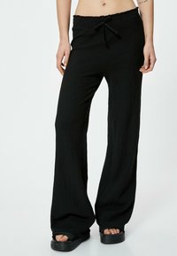 Pantaloni larghi neri con texture, dotati di cintura elastica e cordino. Il tessuto sembra leggero e traspirante.