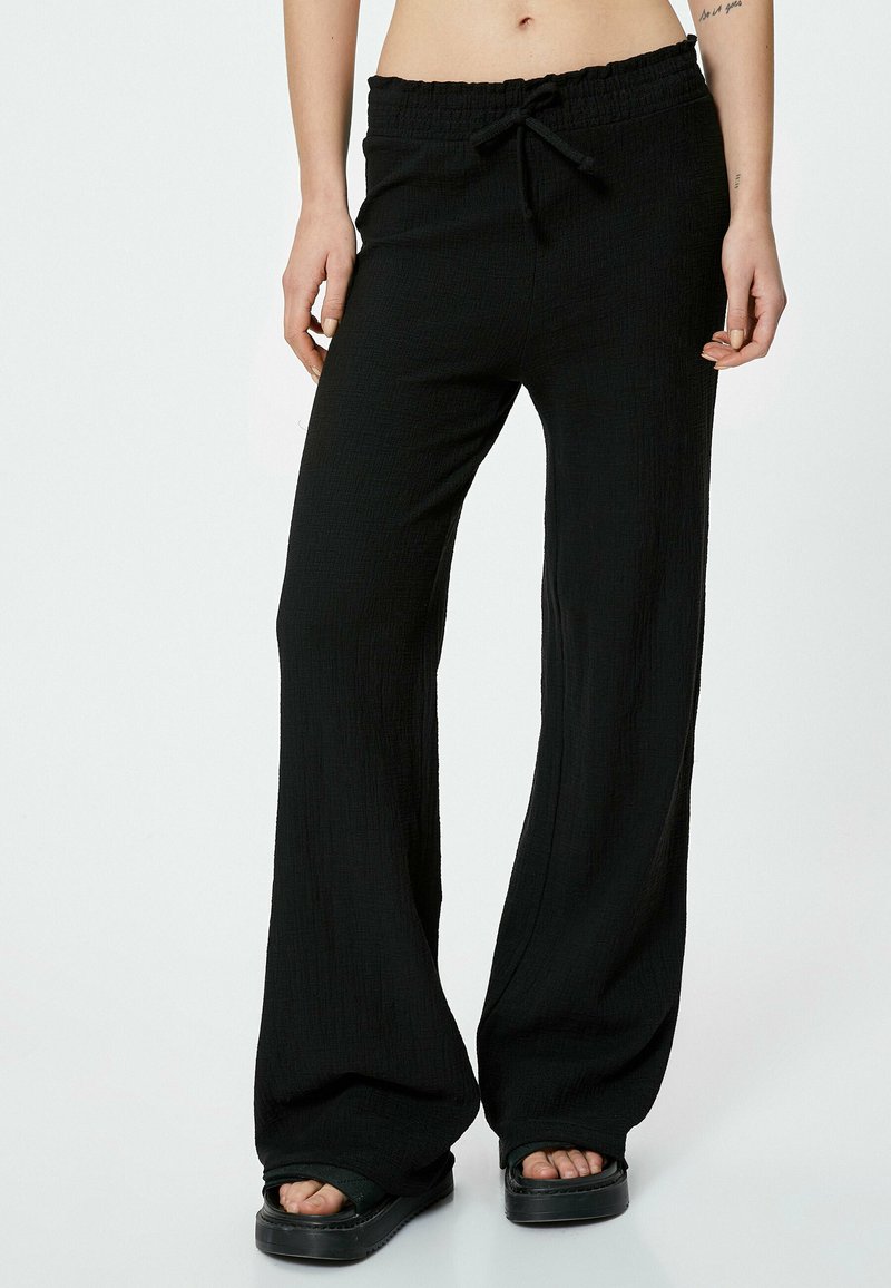 Pantaloni larghi neri con texture, dotati di cintura elastica e cordino. Il tessuto sembra leggero e traspirante.