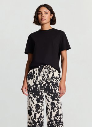 Maglietta nera a maniche corte abbinata a pantaloni a vita alta, ampi, con sfondo crema e motivi a schizzi neri.