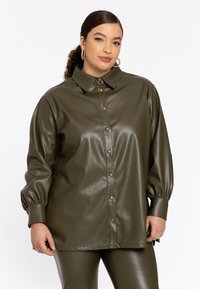 Olijfgroene neplederen overhemdjack met een grote kraag, knoopsluiting aan de voorkant en pofmouwen. Gladde textuur met goudkleurige knopen.