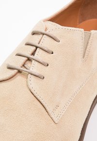 Chaussure oxford en suède beige avec une texture lisse, dotée d'un bout arrondi, de coutures subtiles et d'un lacet à l'avant avec des lacets bicolores.