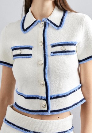 Vit kort jacka med blå och marinblå detalj, med krage, korta ärmar och silverknappar, tillverkad av texturerat tyg.