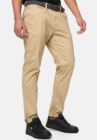 Chinos de algodón beige con un corte recto, que presentan un cinturón negro con estampado, bolsillos y se combinan con zapatillas negras.