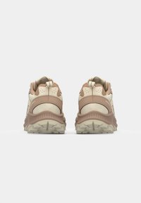 Des baskets beiges et rose pâle avec une tige texturée, un col rembourré et une semelle à motif. Elles sont dotées d'un système de laçage et d'un tirant à l'arrière.