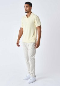 Polo de rayas amarillo claro con mangas cortas, combinado con pantalones beige y zapatillas blancas, presentado sobre un fondo neutro.