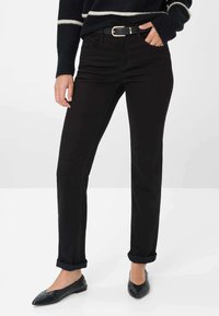 Jeans neri a gamba dritta con orli arrotolati, dotati di cintura con fibbia dorata. Materiale in cotone liscio con tasche laterali. Indossati con scarpe nere senza tacco.