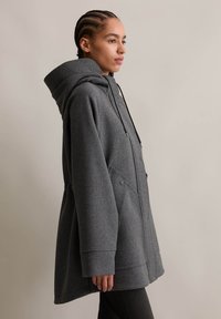 Manteau en mélange de laine gris avec une capuche, doté d'une fermeture éclair à l'avant, de boutons-pression et de poches latérales. Coupe décontractée avec une texture lisse.