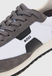 Gray suede and white fabric sneaker with black accents, flat laces, and textured rubber sole; features “BOSS” logo on the side.