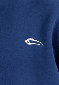 Il tessuto blu navy presenta un logo ricamato bianco sul lato sinistro. La texture è liscia con un motivo di maglia uniforme.