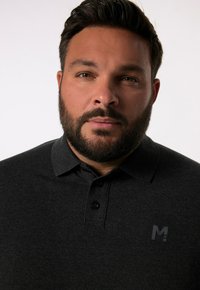 Tmavě šedé polo tričko s límcem, s třemi černými knoflíky a malým vyraženým logem na hrudi. Hladká textilní struktura, těsný střih.
