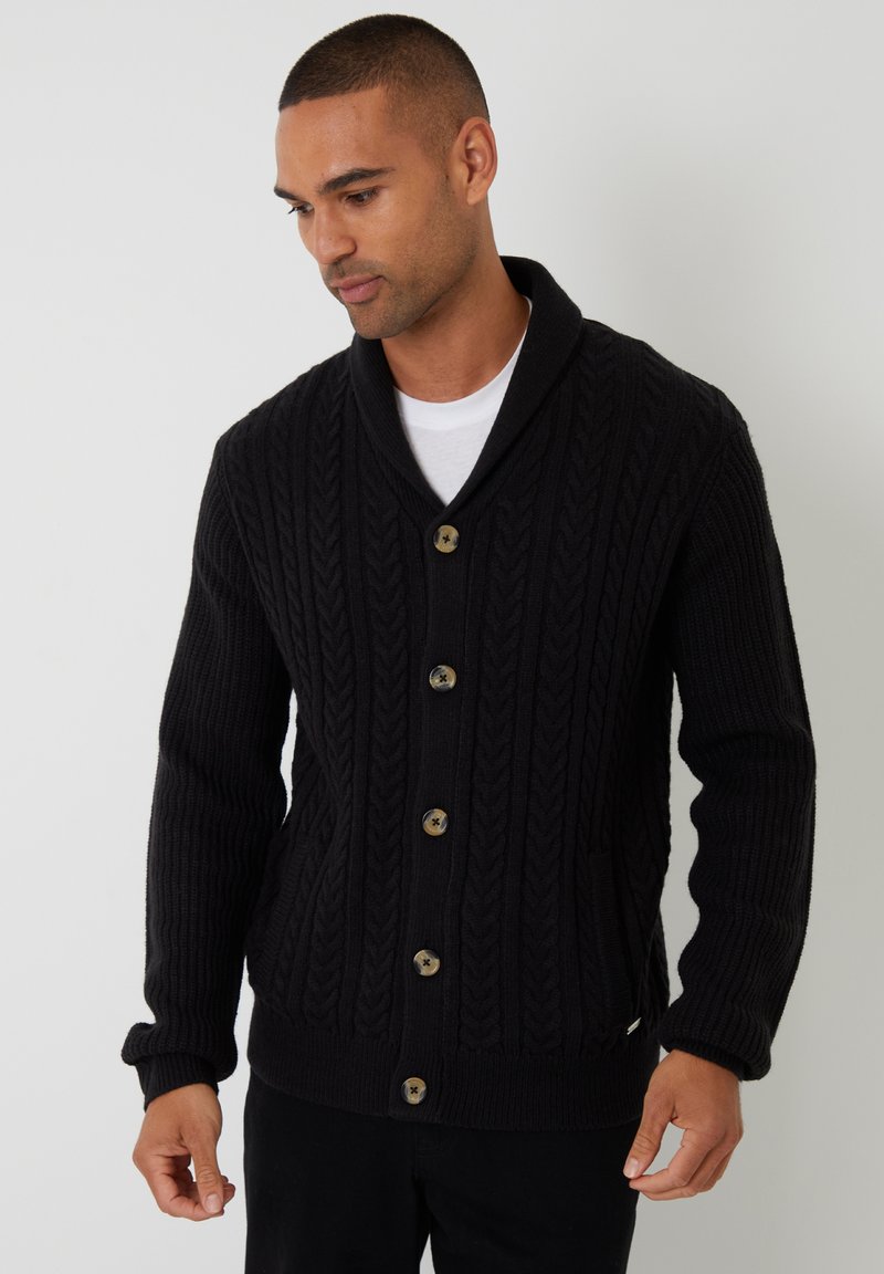 Cárdigan negro de punto con un patrón de trenza, cuello de chal, botones frontales y bolsillos laterales. Los puños y el dobladillo acanalados añaden textura.