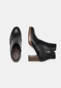 Zwarte leren enkelboots met een ronde neus, zijrits en een bruine, gestreepte blokhak. Met gebogen stiksels als accent.