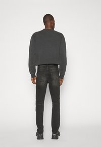 Men's cropped black sweatshirt paired with dark gray skinny jeans. The fabric appears soft, showcasing a simple, smooth design.