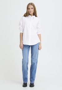 Valkoinen nappipaitakuvio, jossa on hienovaraiset pystysuorat raidat, yhdistettynä vaaleansinisiin suoriin farkkuihin ja mustiin nilkkureihin.