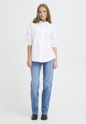 Chemise blanche à boutons avec des rayures verticales subtiles, associée à un jean droit bleu clair et des bottines noires.