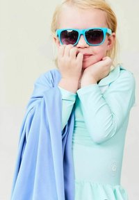 Aquamarine long-sleeve swimsuit with a ruffled hem, paired with a light blue cover-up. Child wears turquoise sunglasses, smiling with hands to face.