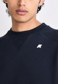 Maglione navy con collo a giro, caratterizzato da un piccolo logo bianco sul lato sinistro del petto. Realizzato in una morbida miscela di cotone con una texture liscia.