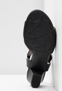 Svart högklackad sandal med en strukturerad gummisula, flera remmar och en solid klack, märkt med storlek 37.