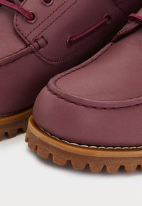 Close-up van kastanjebruine leren laarzen met dikke bruine rubberen zolen en bijpassende kastanjebruine veters die door metalen oogjes zijn geregen.