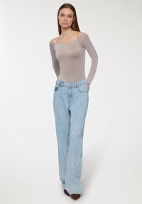 Jasnobeżowy body z długim rękawem o szerokim dekolcie, zestawione z jasnoniebieskimi, wysokim talią spodniami typu wide-leg, posiadającymi teksturowane wykończenie denimu.