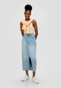 Helles blaues Jeansrock mit einem Schlitz vorne und hoher Taille, kombiniert mit einem weiß-orange gestreiften Tanktop und einem pfirsichfarbenen Pullover, der um die Schultern gebunden ist.
