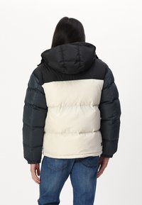 Chaqueta de plumas con capucha negra, sección media crema y mangas azul oscuro, con puños elásticos y cuello alto.