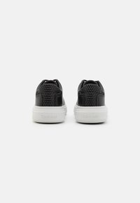 Sneakers negre cu textură împletită, accente din piele netedă și tălpi din cauciuc alb. Prezintă logo-ul Calvin Klein pe călcâi.