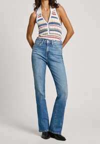 Blusa senza maniche a righe con colletto, caratterizzata da colori blu, rosso e crema; abbinata a jeans svasati blu chiaro e stivali neri.