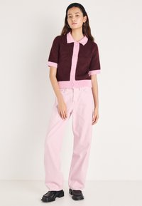 Bordozsarkana īsroku džempers ar rozā apkakli un akcentiem, kombinēts ar gaiši rozā plaša piegriezuma džinsiem un melnām kurpēm ar papēžiem.