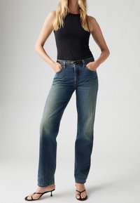 Modré džíny s vysokým pasem ve volném střihu s vybledlým umytím, pár zadních kapes a černým pásem, nošeny s černým tílkem a sandály.