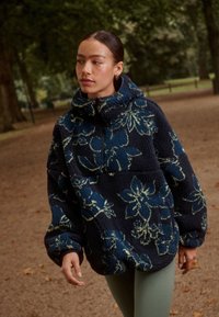 Czarna bluza polarowa z kwiatowym wzorem w odcieniach niebieskiego i zielonego, z wysokim kołnierzem i półzamkiem, o pluszowej fakturze.