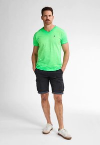 Grønstribet v-hals t-shirt kombineret med sorte cargoshorts og hvide sneakers. T-shirten har et logo på brystet og en blød tekstur.