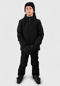 Schwarze, isolierte Skijacke mit Frontreißverschluss, passende schwarze Handschuhe, Schneehose und Skischuhe; getragen von einem Kind. Mütze auf dem Kopf.